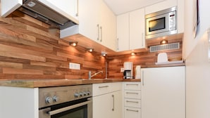 A compact kitchen with a built-in oven, a microwave, and a coffee maker. - Ferienwohnung in Wyk-boldixum auf Foehr (Wyk auf Foehr)