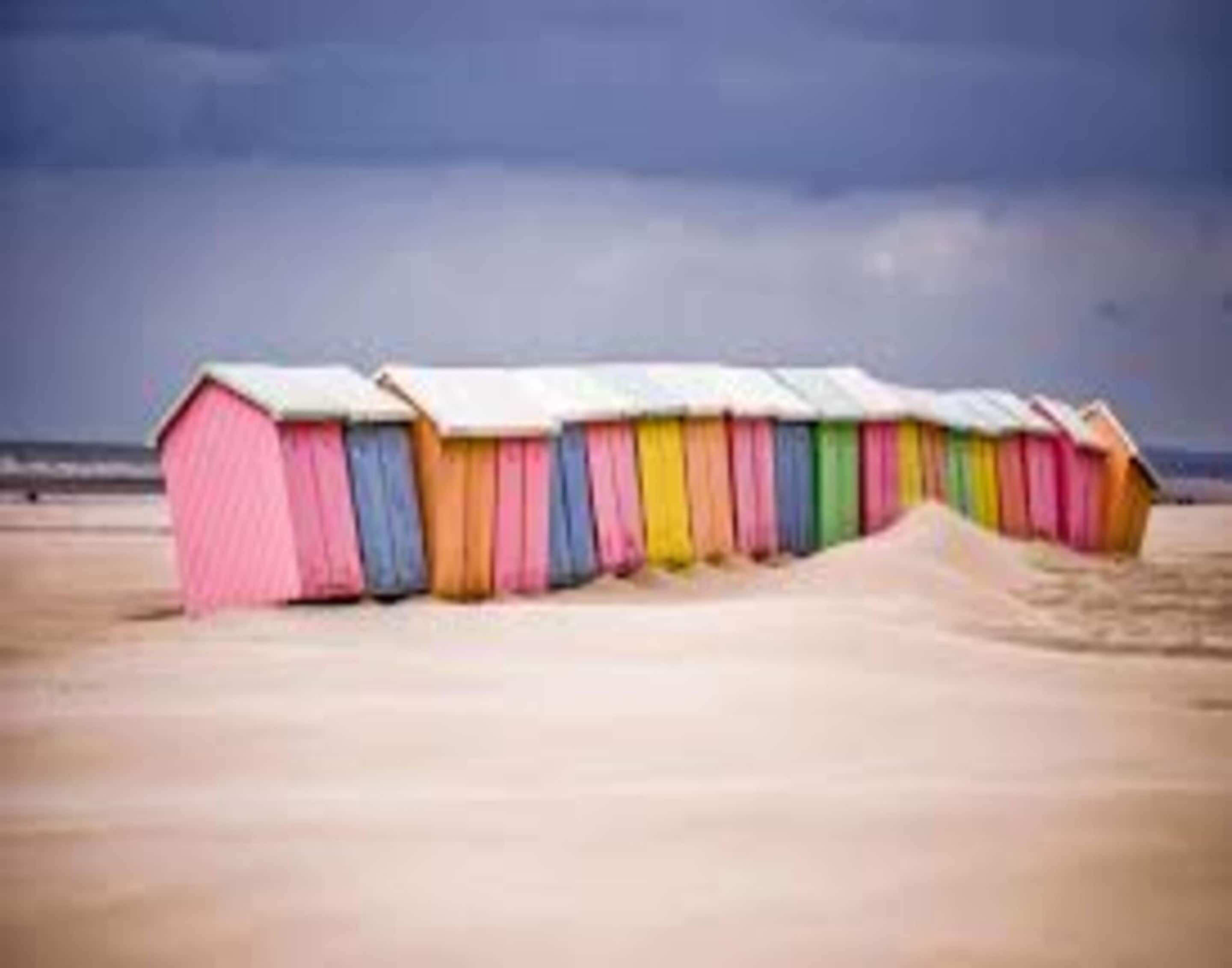 Una hilera de cabañas de playa frente a una arena y el océano al fondo.