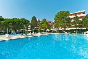 A swimming pool with lounge chairs and umbrellas, surrounded by trees and buildings. - Residence Valbella Beach (San Michele al Tagliamento)