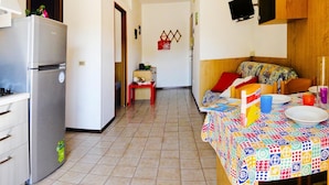 A compact kitchen with a refrigerator, a dining area with a table set for two, and a small red stool. - Residence Valbella Beach (San Michele al Tagliamento)