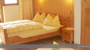 Un lit en bois avec une couvre-lit à carreaux et des oreillers, une table de chevet et une lampe fixée au mur.