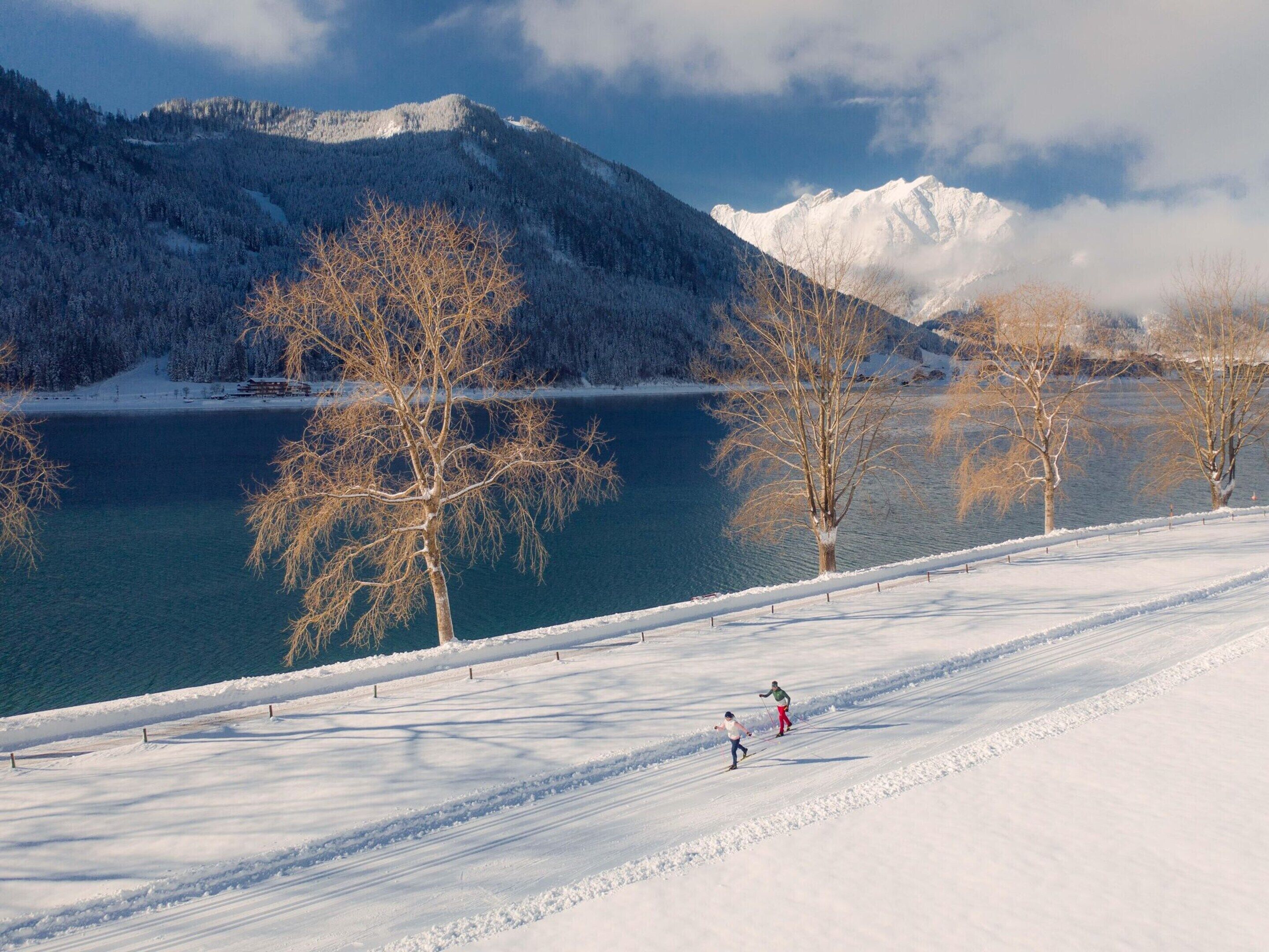 A snow-covered landscape with a lake, trees, and mountains in the background.