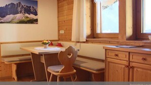 L’intérieur d’un chalet en bois, avec une table à manger, des bancs et une fenêtre avec des rideaux.