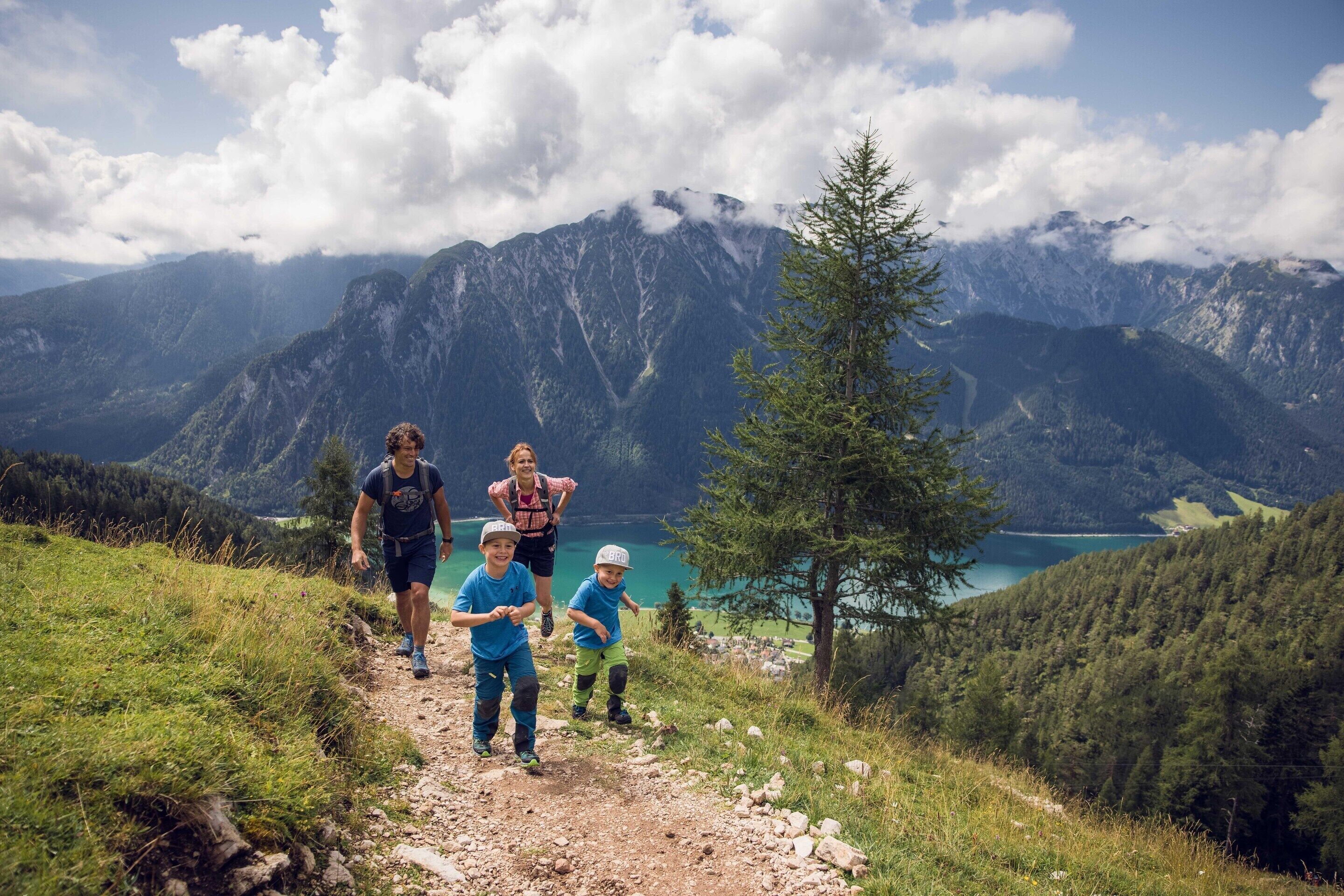 Eine Gruppe Wanderer auf einem Bergpfad, mit einem See und Bergen im Hintergrund.