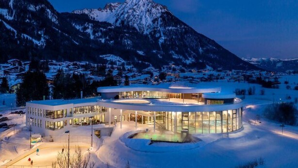 Un bâtiment moderne doté d’un espace central circulaire, entouré d’un paysage enneigé et avec des montagnes en arrière-plan.
