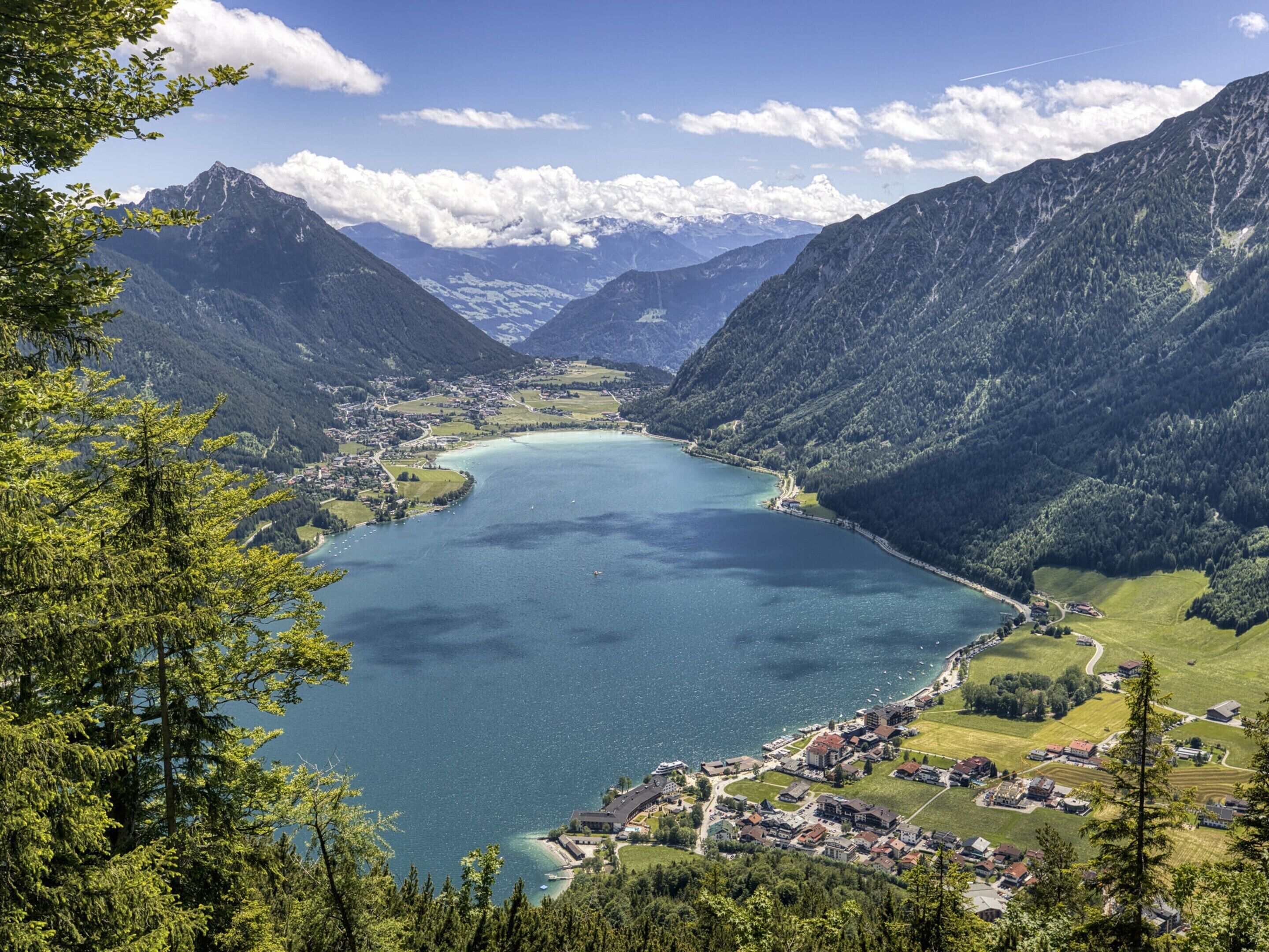 A mountainous landscape with a lake, a small town, and surrounding forested areas.