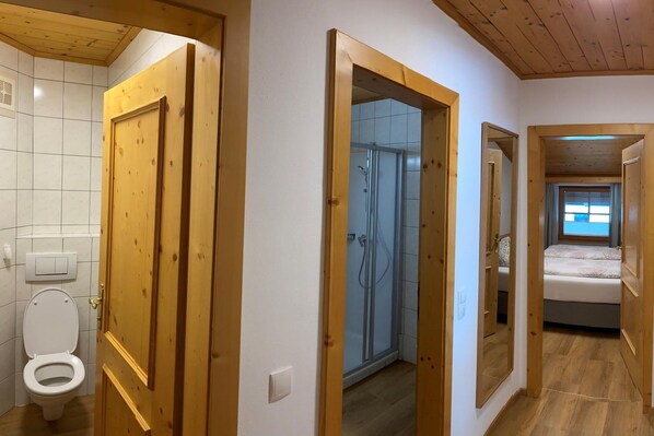 Une pièce avec une porte en bois, des toilettes, une douche et un lit près d’une fenêtre.