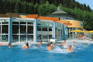 Un espace piscine doté d’un bâtiment entièrement vitré, d’un espace de repos couvert et d’un décor naturel composé d’une forêt.