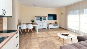 Un salon moderne comprenant un coin cuisine, une table à manger avec des chaises, un téléviseur fixé au mur et un canapé.