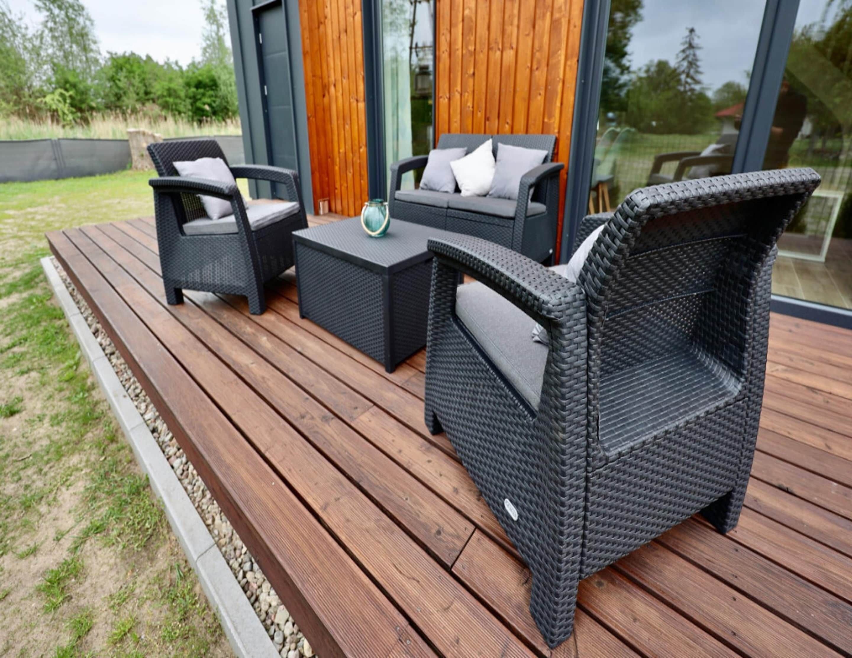 A modern outdoor seating area with wicker furniture and a glass door leading to a wooden interior.