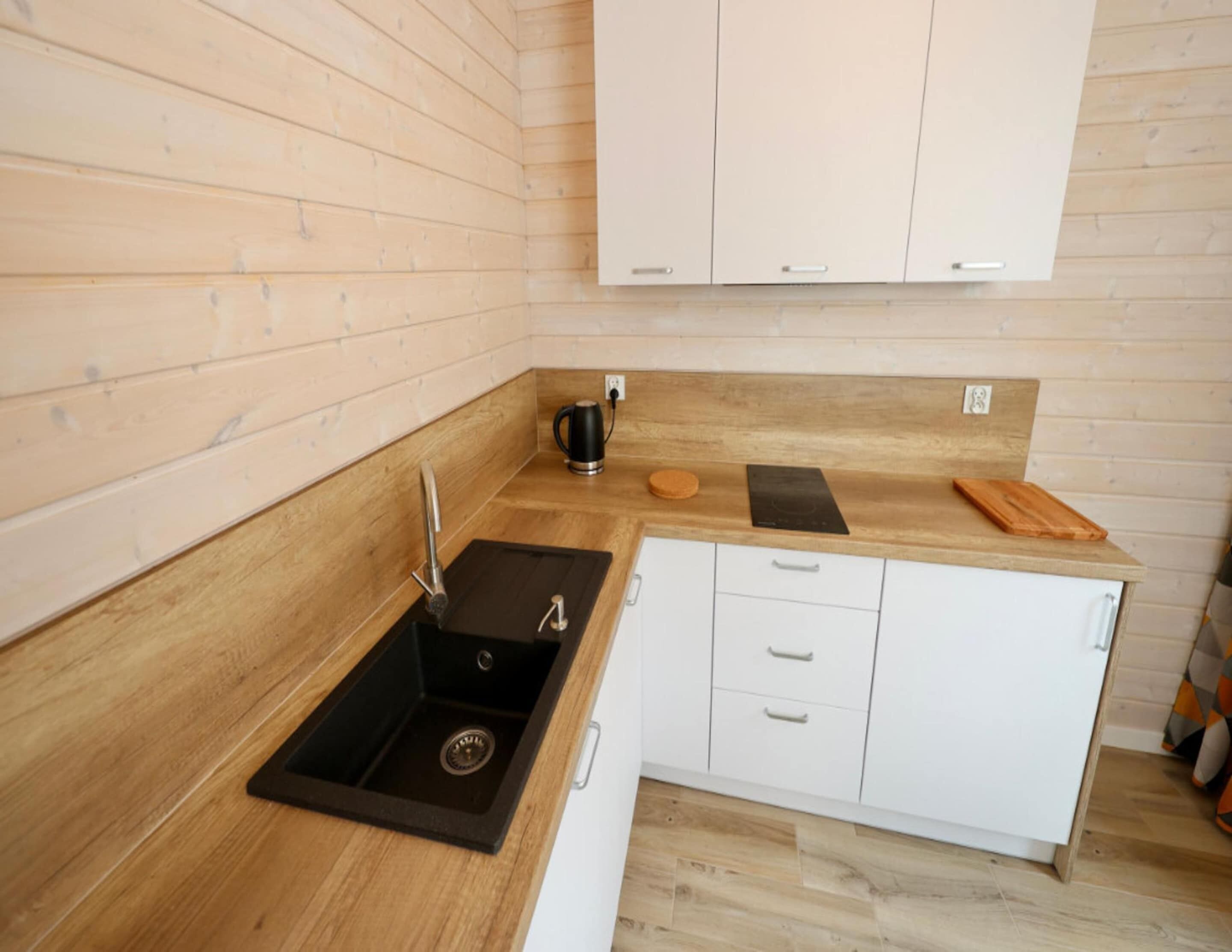 A modern kitchen with wooden cabinetry, a black sink, and a countertop with a kettle and cutting board.
