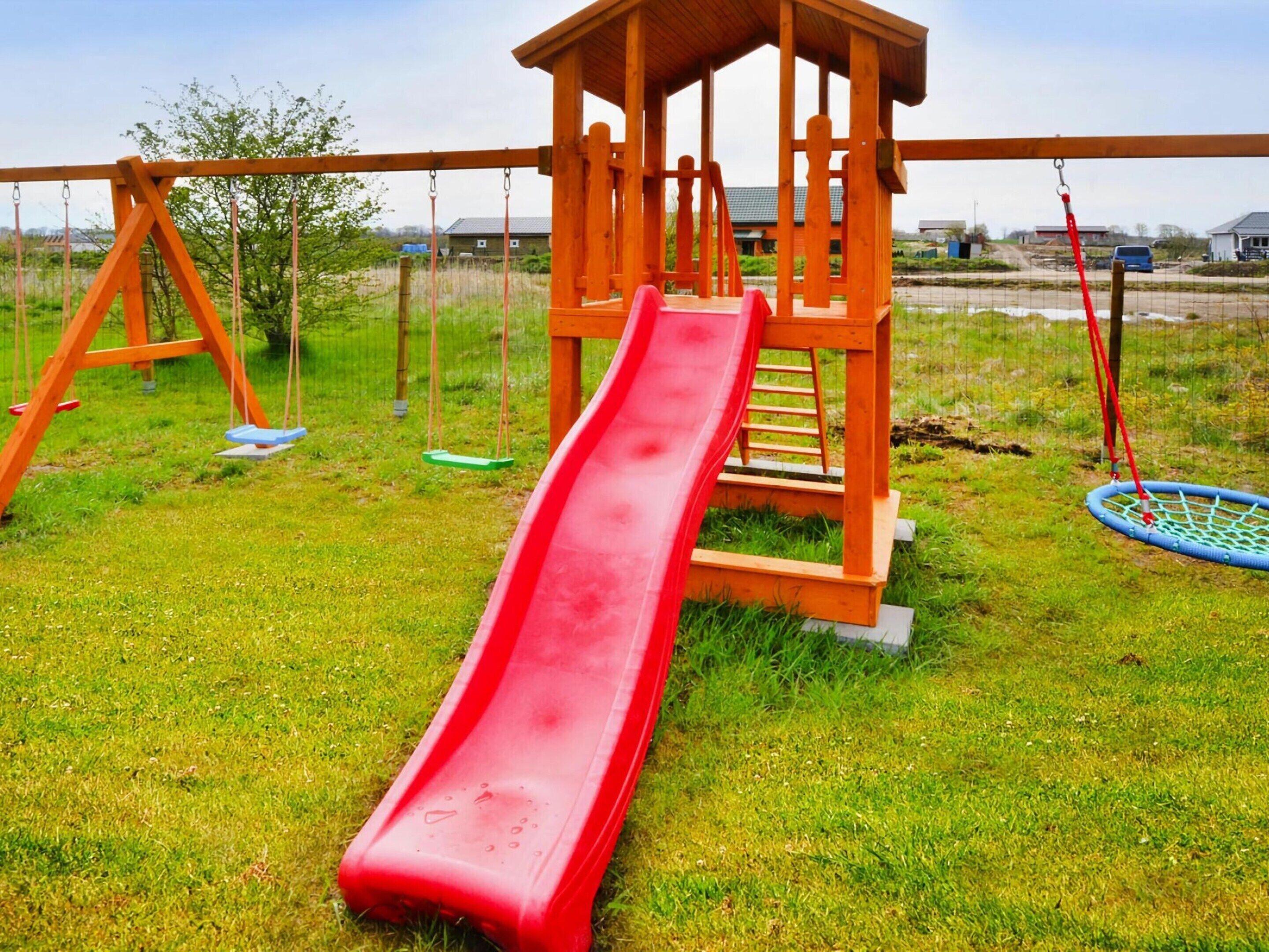 A playground with a red slide, swings, and a wooden climbing structure.