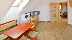 A compact kitchen with a microwave and toaster, a wooden dining table with chairs, and a sloped ceiling with a skylight. - Apartment With a Playground, Close to the Beach (Mielno)