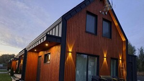 Eine moderne Holzblockhütte mit Terrasse, großen Fenstern und Sitzgelegenheit im Freien.