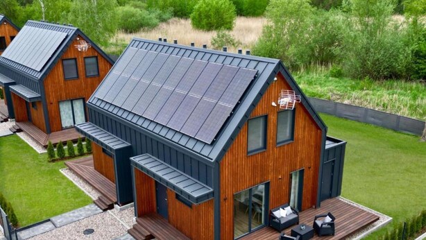 Ein modernes, zweistöckiges Haus mit geneigtem Dach, Solaranlage und einer Terrasse mit Gartenmöbeln.