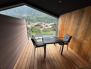 Ein Balkon mit Tisch und Stühlen, Holzboden und Blick auf ein Wohngebiet sowie Berge.