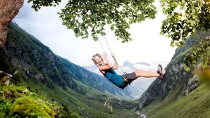 Una persona se balancea en una cuerda en una zona montañosa con un río y vegetación.