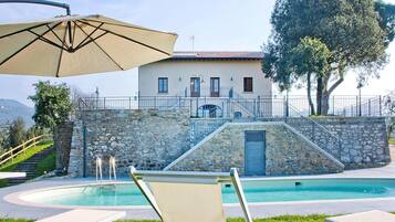A pool area with lounge chairs, a stone wall, and a building with a tiled roof.