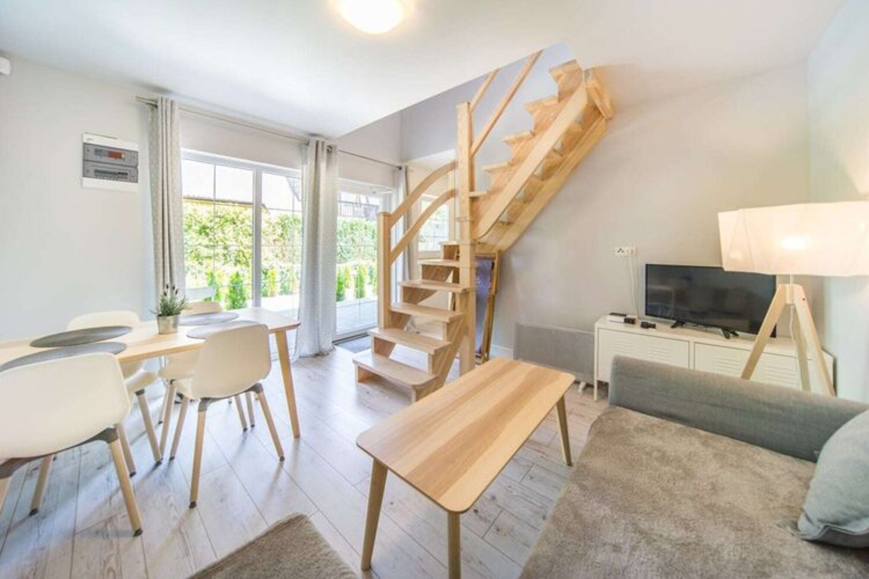 Un salon moderne avec un escalier en bois, un coin repas avec une table et des chaises, un canapé, un téléviseur et une lampe.
