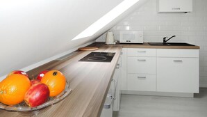 Ett modernt kök med en bänkskiva i trä, en inbyggd mikrovågsugn, en diskho och en fruktskål med apelsiner och äpplen.