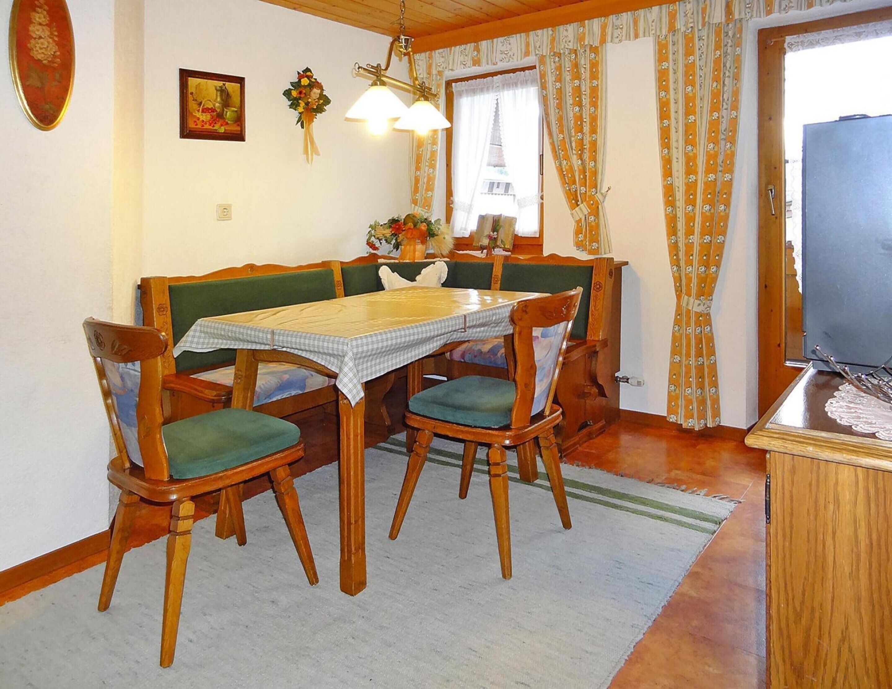 A dining area with a wooden table and chairs, a bench, a chandelier, and a view of a building through the window.