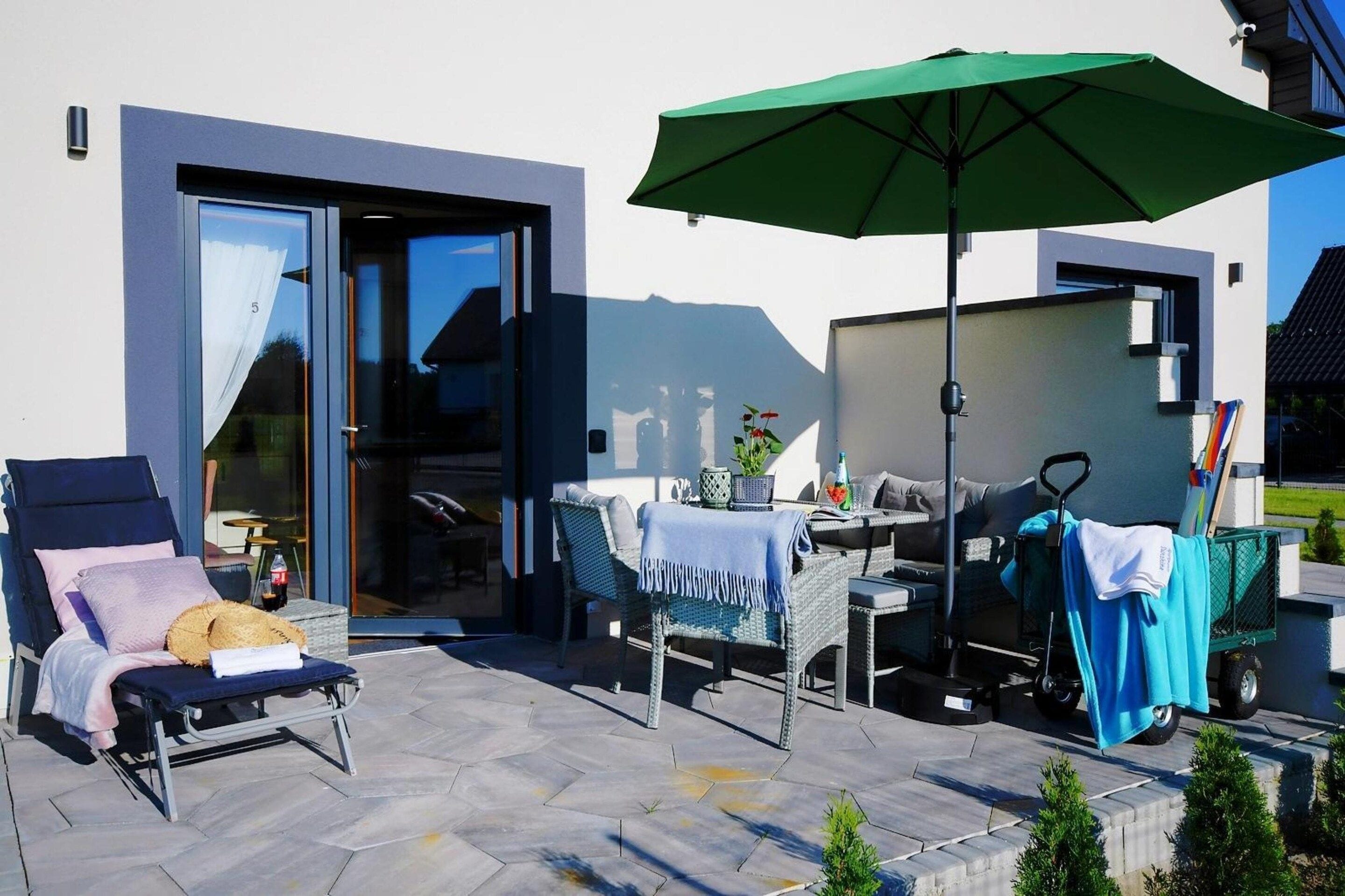 A patio with outdoor furniture, a green umbrella, and a glass door leading to an interior space.