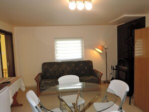 A living room with a round glass table, two white chairs, a patterned sofa, a window with blinds, and a fireplace.