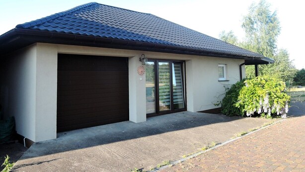 A single-story house with a dark brown garage door, a small window, and a covered porch area. - Holiday Home in a Quiet Location in Borzyslawiec (Goleniow)