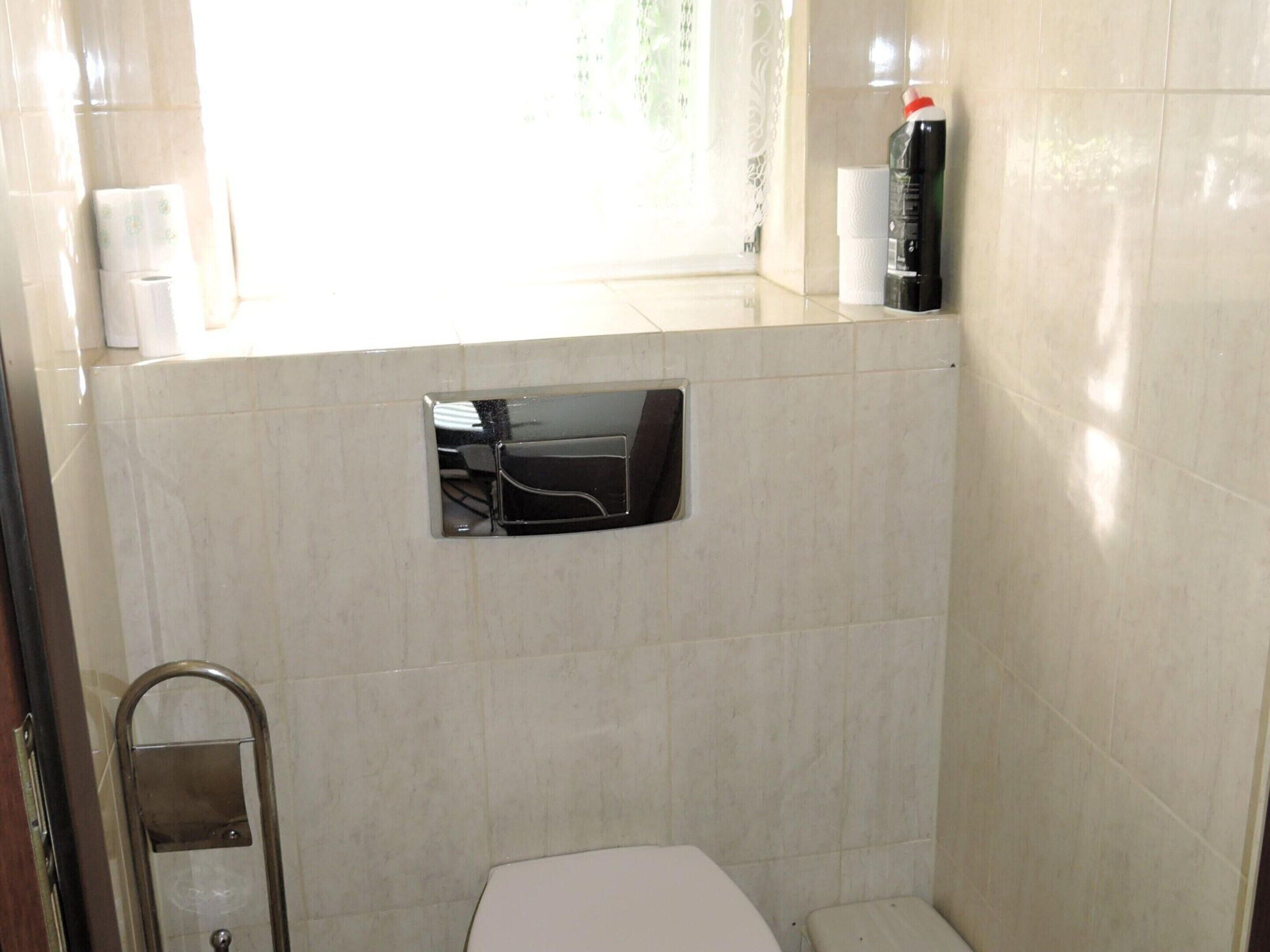 Et lille badeværelse med fliser, toilet, gelænder og et vindue.