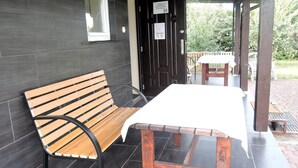 A wooden bench and table set on a tiled patio with a dark wall and a door with signs. - Holiday Home in a Quiet Location in Borzyslawiec (Goleniow)