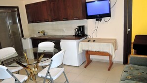 A compact kitchen with wooden cabinets, a glass dining table, white chairs, a small wooden stool, and a television mounted on the wall. - Holiday Home in a Quiet Location in Borzyslawiec (Goleniow)