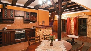 A kitchen with dark wooden cabinets, a stone wall, and a dining area with a table and chairs. - Apartment in Darlowo Near Seaside Beach (Darlowo)