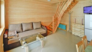A wooden interior with a sofa, a glass coffee table, a TV, and a kitchen area with a refrigerator. - Comfortable Holiday Homes Close to the Beach (Mielno)