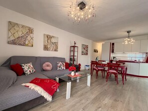 A modern living room with a grey sofa, red cushions, a glass coffee table, and a red throw blanket. There is a dining area with red chairs and a kitchen in the background. - Apartment, Los Llanos de Aridane (Los Llanos de Aridane)