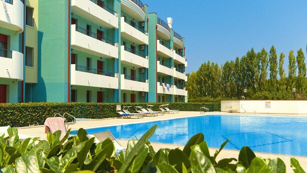 A multi-story hotel with a swimming pool, balconies, and a well-maintained garden.