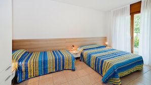 A hotel room with two beds, a wooden headboard, a nightstand with a lamp, and a window with curtains.
