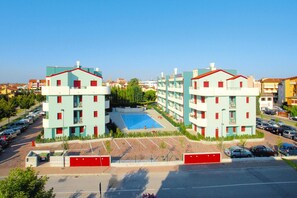 A multi-story hotel with a central swimming pool, surrounded by parking spaces and greenery. - Apartment in Caorle With Heating (Caorle)