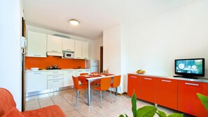 A modern kitchen with white and orange cabinets, a dining table with orange chairs, and a television on a cabinet.