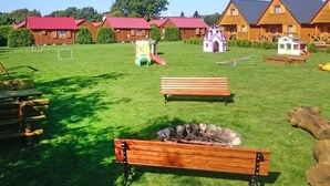 A grassy area with wooden benches, a small fire pit, and play structures. - Holiday Homes With Terraces, Close to the Beach (Postomino)
