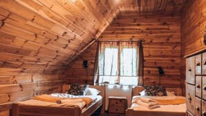 A cozy cabin-style room with wooden walls and a sloped ceiling. There are two beds with matching headboards and a small table between them.