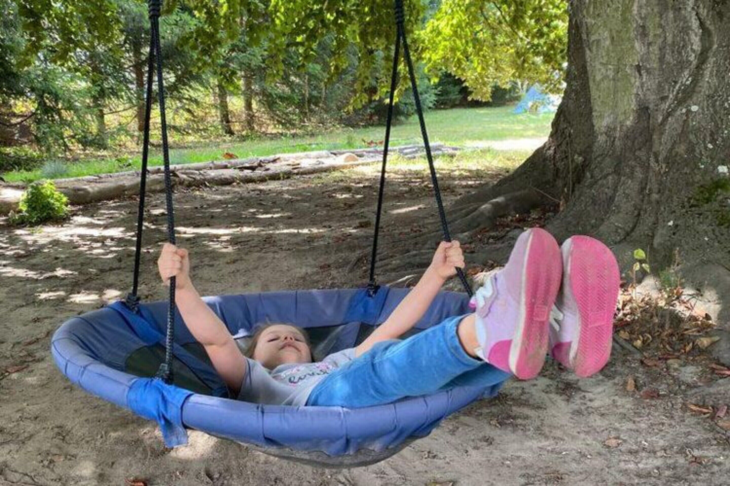 A child in a blue hammock swing attached to a tree, with a natural outdoor setting in the background.