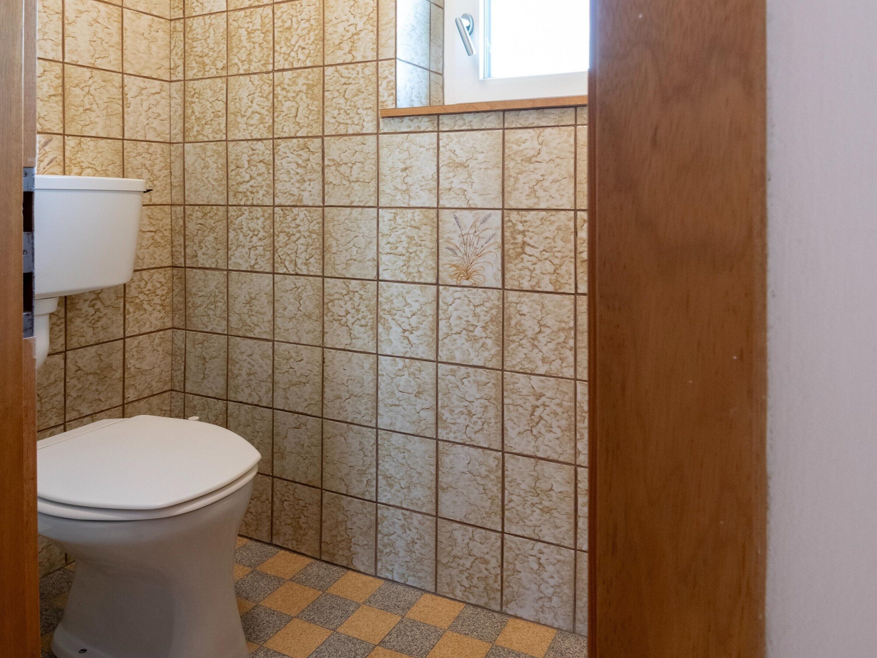 Un baño con inodoro, paredes de azulejos y piso a cuadros.
