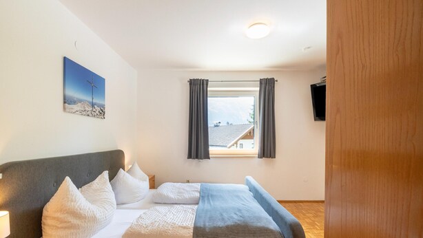 A bedroom with a bed, a bedside table, a nightstand, a window with curtains, a wall-mounted TV, and a painting. - Chalet in Fugen Near Spieljochbahn (Fuegen)