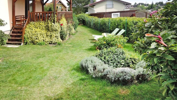 En välskött trädgård med en träaltan, en gräsmatta och olika typer av buskar.