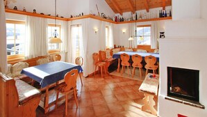 A cozy room with a wooden ceiling, a dining table with chairs, a fireplace, and a window with curtains.