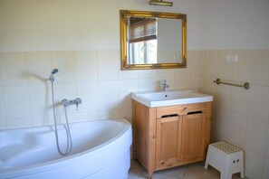 A bathroom with a white bathtub, wooden vanity, and a gold-framed mirror. - Large Holiday House With Terrace, Bobolin (Darlowo)
