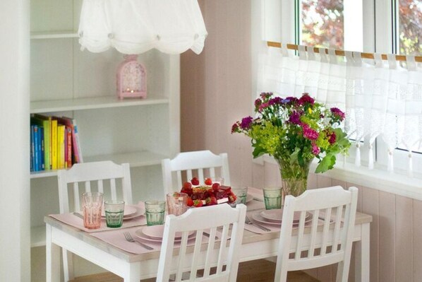 Une table à manger avec des chaises blanches, un vase de fleurs et une assiette de fraises.