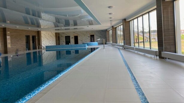 A spacious indoor swimming pool with a marble wall and a reception desk.