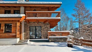 A log cabin with a stone entrance, wooden balcony, and snow-covered surroundings. - Chalet in Saalbach With Panoramic Sauna (Saalbach-Hinterglemm)