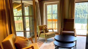 A cozy room with a large window, a wooden chair, a smaller armchair, and a round table. - Chalet in Saalbach With Panoramic Sauna (Saalbach-Hinterglemm)